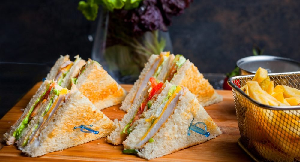 Side view club sandwich with french fries in wooden serving board on dark stone background